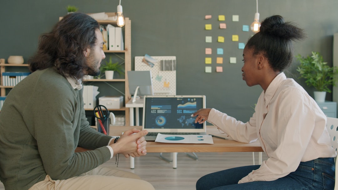Two colleagues discussing data on a laptop screen.