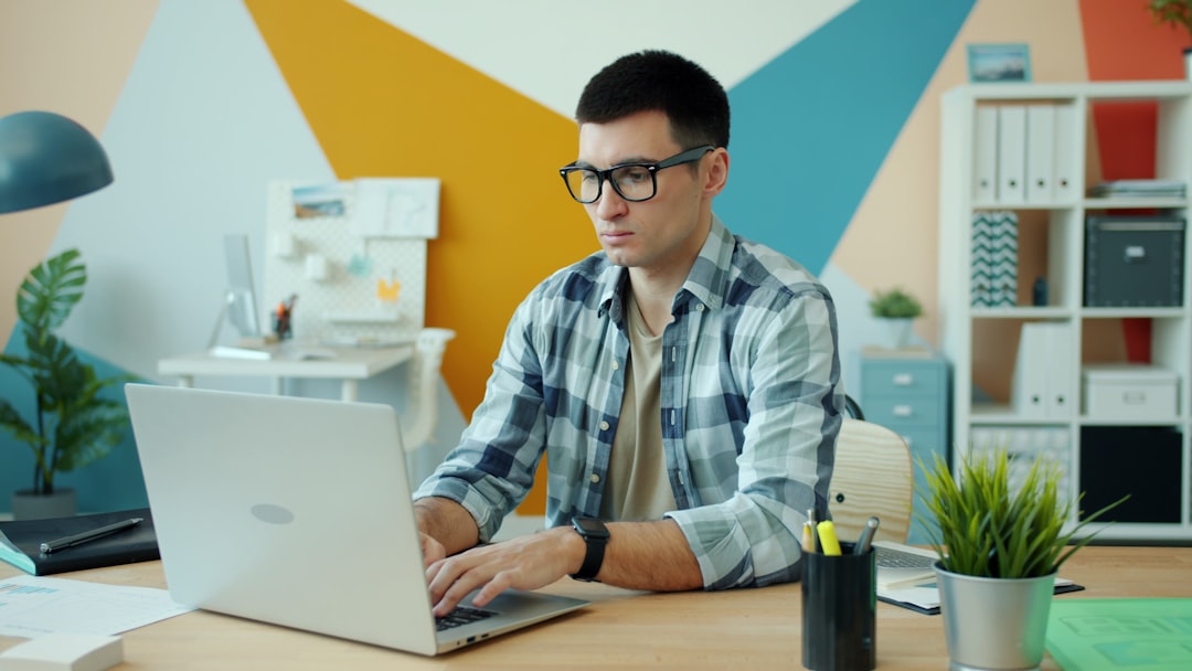 Man wearing glasses typing on laptop at desk.