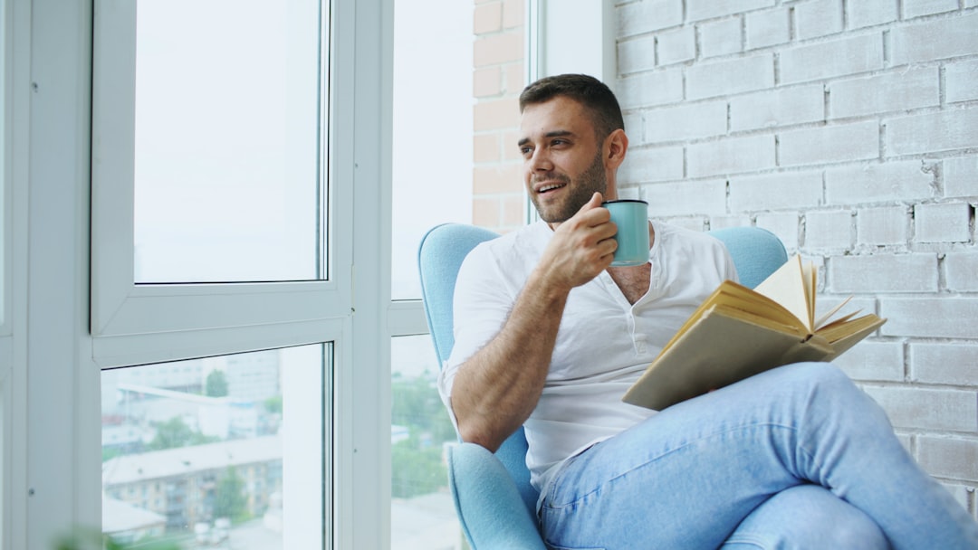 Man reading a book and drinking coffee by window