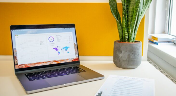 a laptop computer sitting on top of a desk next to a plant
