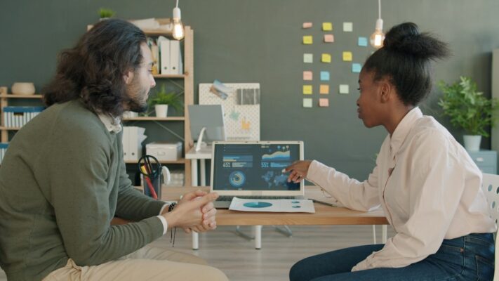 Two colleagues discussing data on a laptop screen.