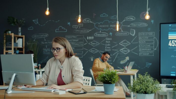 Woman working on computer in modern office with chalkboard.