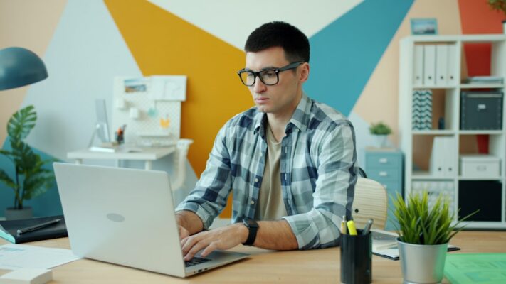 Man wearing glasses typing on laptop at desk.